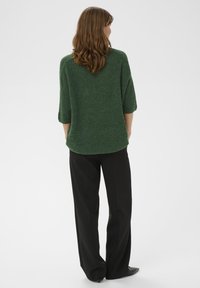 Grüner, strukturierter Strickpullover mit 3/4-Ärmeln, kombiniert mit hoch taillierter schwarzer Hose. Weiche, legere Passform und midilanger Schnitt.