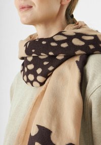 Écharpe marron et beige avec un motif à pois, fabriquée en tissu doux, drapée autour du cou, mettant en valeur la texture et le contraste des couleurs.