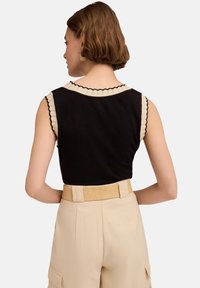 Czarny top bez rękawów z falbaniastym beżowym kołnierzem, zestawiony z beżowymi spodniami o wysokim stanie i teksturowanym paskiem, widok z tyłu.