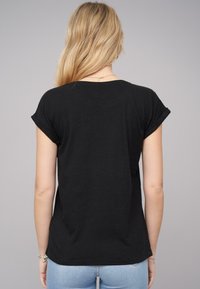 Svart kortärmad t-shirt i bomull med avslappnad passform och uppvikta ärmslut, sedd bakifrån mot en neutral bakgrund.