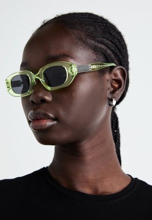 Groen getinte zonnebril met een slank, rechthoekig frame en donkere lenzen; gestructureerde grijze armen met branding. Glad huid en een zwart shirt.