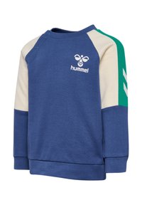 Blaues Sweatshirt mit beigen und türkisfarbenen Raglanärmeln, ausgestattet mit einem Druckknopf an der Schulter und einem weißen Logo auf der Brust. Baumwollmaterial.