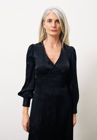 Schwarzes Kleid mit V-Ausschnitt, langen Puffärmel und mit Stoff überzogenen Knöpfen auf der Vorderseite. Glattes, strukturiertes Material mit einem dezenten Muster.
