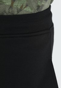 Mustavad sportlikud püksid soonikkoes vöökohtadega, pehme tekstuur ja hästi istuv disain. Pilt näitab üleminekut vöökoha ja pükste vahel.