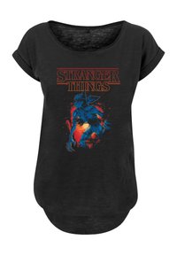 Black short-sleeve T-shirt featuring a blue monster graphic, red accents, and the text "STRANGER THINGS" in bold, orange lettering.