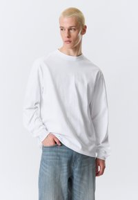 Langærmet hvid bomulds-T-shirt med rund halsudskæring, løstsiddende pasform og tilspidsede ærmer, kombineret med lyseblå denimjeans.