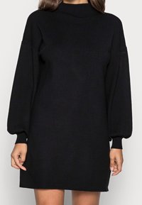 Svart tröjklänning med hög hals, ballongsärmar och ribbade muddar; tillverkad av mjukt stickat material; knälång design.