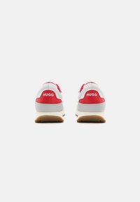 Rote und weiße Sportschuhe aus einem glatten Material. Ausgestattet mit einem Logo an der Ferse, strukturierten Mustern und einer Gummisohle.