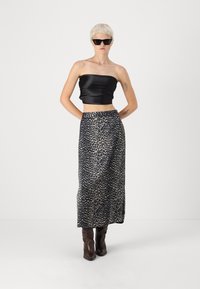 Fekete selyem, pánt nélküli crop top, hosszú, leopárdminta szoknyával párosítva. A modell sötét napszemüveget és barna, térd fölé érő csizmát visel.