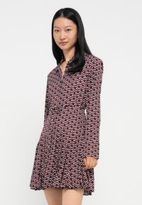 Garais piedurkņu kleita dziļi sarkanā krāsā ar abstraktu baltu un rozā rakstu, ar sasprindzinātu jostasvietu un izplestu svārku, ar pogu detaļām apkaklē.