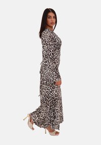 Robe maxi à imprimé léopard en tissu léger. Manches longues, buste ajusté, jupe évasée, fentes latérales, et associée à des talons ouverts.