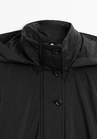 Giacca leggera nera con colletto alto, caratterizzata da chiusura con zip e quattro dettagli a bottone sulla parte frontale; tessuto liscio e strutturato.