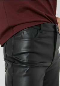 Pantalons en simili cuir noir au design ajusté, dotés de poches latérales et de détails de couture visibles. Portés avec un haut bordeaux.