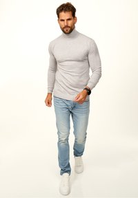 Gray turtleneck sweater in a knit texture, paired with light blue jeans and white sneakers. The fit is slim, emphasizing a casual look.