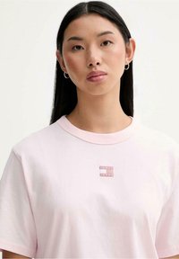 T-shirt in cotone rosa chiaro con scollo rotondo, caratterizzata da un piccolo logo ricamato sul petto. Maniche corte e forma ampia.