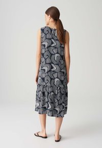 Ärmelloses navy Kleid mit weißem abstraktem Wellenmuster, rüschensaum und lockerer Passform; aus einem leichten Stoff gefertigt.