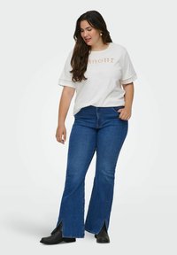 T-shirt bianco a maniche corte con dettagli in pizzo e testo "Amour", abbinato a jeans svasati blu con orli a spacco e stivaletti neri alla caviglia.