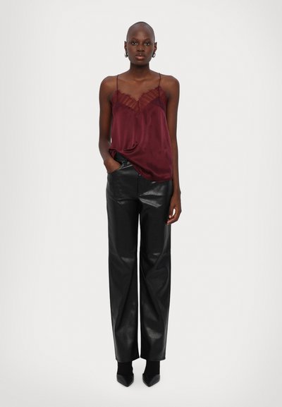 Bordeaux satijnen camisole met kantafwerking, gecombineerd met hoge zwarte leren broek. Model staat rechtop met handen in de zakken.