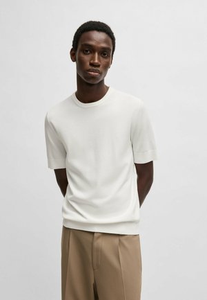 Short-sleeve cream knit sweater with a crew neckline and ribbed cuffs. Worn with beige pleated trousers, minimalistic design.