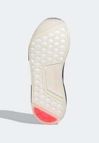 Gummisneakersula med ett vitt hexagonalt mönster, med en r öd accent vid hälen och en strukturerad greppyta för bättre fäste.