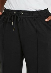 Svarta dragkedjeshorts i ett texturerat tyg, med resår i midjan, ögon av guldton och sidofickor för funktionalitet.