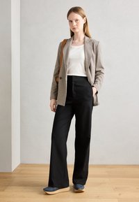Blazer z vzorom houndstooth, biela tielko, čierne široké nohavice a modre topánky s svetlo čistom podošvom. Modelka drží hnedú ramennú tašku.