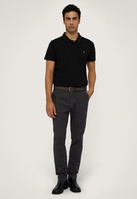 Czarna koszulka polo z kontrastowym kołnierzykiem, zestawiona z ciemnoszarymi spodniami. Model nosi czarne botki za kostkę i brązowy pasek.