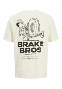 Tegneserie mekaniker står ved siden af et stort dæk med værktøj, over fed tekst "BRAKE BROS Classic Garage" og kontaktoplysninger på en hvid T-shirt.