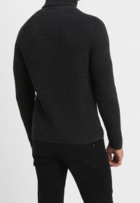 Pull à col roulé côtelé gris foncé avec une coupe ajustée, un tissu texturé et un design de manches sans coutures. Porté avec un pantalon noir.