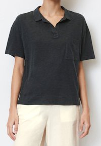 Schwarzes kurzärmliges Poloshirt aus weichem Material, mit einer Tasche auf der linken Brust und einer lockeren Passform.