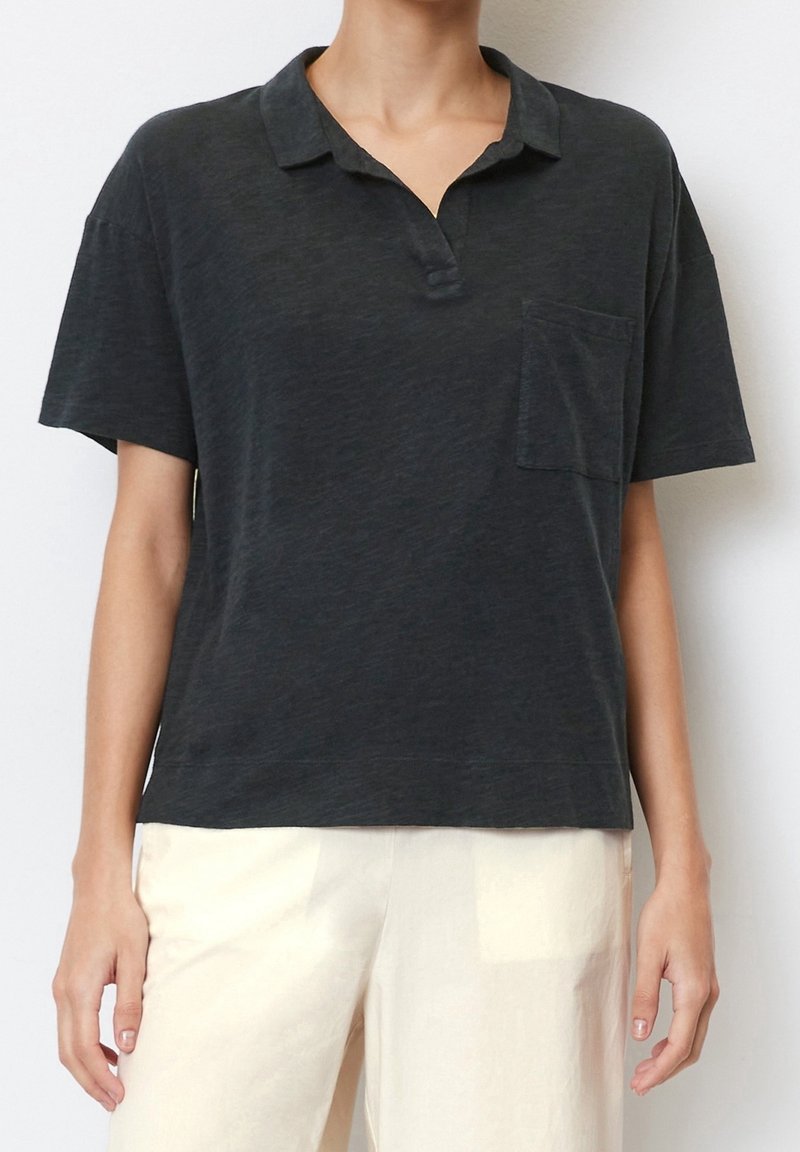 Schwarzes kurzärmliges Poloshirt aus weichem Material, mit einer Tasche auf der linken Brust und einer lockeren Passform.