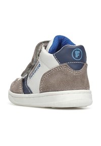 Sneaker con tomaia in suede grigio e pelle bianca, fodera in tessuto blu e una patta in velcro. Presenta una suola in gomma bianca e un dettaglio con logo.
