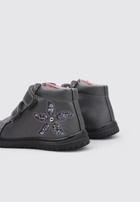 Bottes pour enfants de couleur gris foncé, équipées d'un design de fleurs pailletées sur le côté et de sangles Velcro, présentées de profil et de l'arrière.