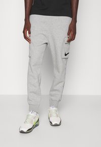 Grå bomullssweatpants med sidofickor, svart Nike-logga och kontrasterande sidostripes. Kombineras med vita och neongröna sneakers.