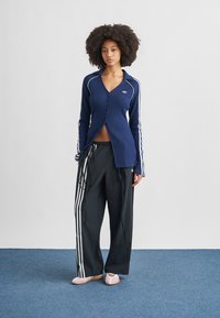 Navy ribbed cardigan with buttons, white stripes on sleeves; paired with black sweatpants featuring three white stripes on sides.