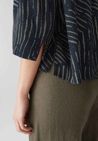 Marineblause mit hellgrauen vertikalen Streifen, entspannt geschnitten mit seitlichen Schlitzen, kombiniert mit hellolivgrünen strukturierten Hosen.