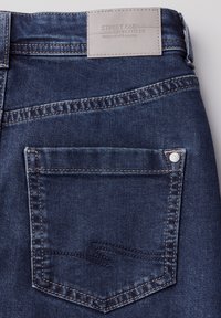 Mörkblå denimjeans med en läderetikett som säger "STREET ONE" på bakdelen av midjan. Har en bakficka med subtila sömnadsdetaljer.