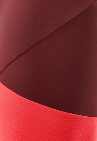 Tissu de sport rouge et bourgogne avec une finition lisse et mate, accompagné d'une bande tissée rouge texturée le long du bord inférieur.