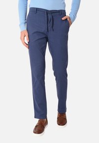 Pantaloni blu scuro in cotone con una vestibilità rilassata, dotati di coulisse e tasche laterali, abbinati a scarpe marroni.