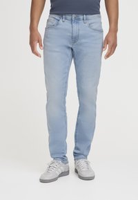 Jeans din denim de culoare albastră deschis, cu o croială slim, design cu cinci buzunare și decolorări subtile. Asortate cu pantofi sport gri.