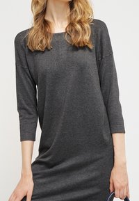 Szara, luźna sukienka z rękawami o długości trzech kwart, okrągłym dekoltem, wykonana z miękkiego materiału; charakteryzuje się drapowaną konstrukcją i subtelną fakturą.