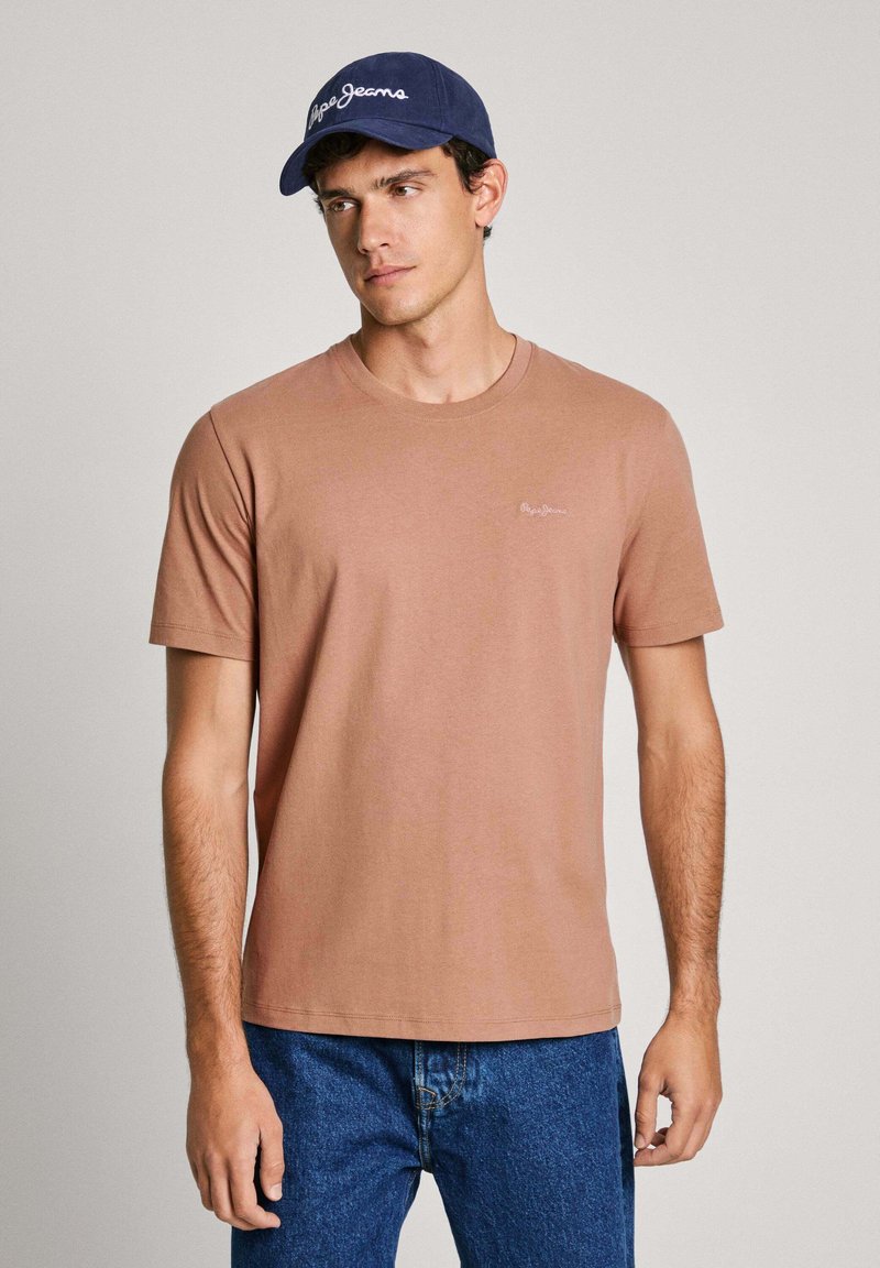 Camiseta de algodón marrón claro con mangas cortas y cuello redondo, combinada con una gorra azul marino que muestra el logo en blanco de "Pepe Jeans".