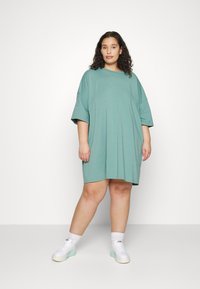Vestido T-shirt oversized em verde menta, feito de algodão suave. Apresenta mangas curtas, um corte descontraído e um decote redondo. Usado com ténis brancos.