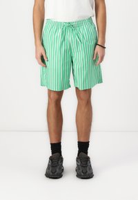 Green and white vertically striped swim shorts with an elastic waistband and drawstring. Worn with black socks and dark athletic shoes.