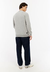 Grijze sweatshirt met geribbelde manchetten en tailleband, gecombineerd met donkerblauwe losse jeans. Zichtbaar logotag op de linkse heup.