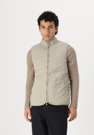 Beige quilted vest with a high neck and front zip, featuring side pockets and textured brown sleeves. Simple, modern design without patterns.