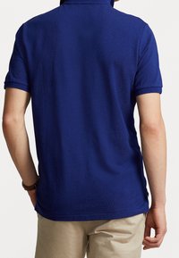 Modrá polokošile, krátké rukávy, textura látky, plochý límec. Má rovný spodní lem a jemný pletený vzor.