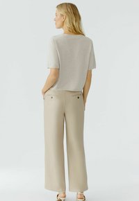 Lichtgrijze trui met korte mouwen, een ronde halslijn en rechte pasvorm, gecombineerd met beige wijde broek met twee achterzakken en subtiele knopen.