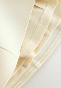 Nærbillede af lagdelt beige stof med overlock-søm og glatte sømme, der fremhæver tekstur og konstruktionsdetaljer.