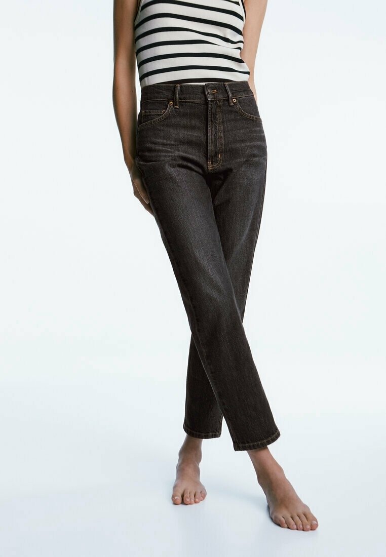 Jeans in denim scuro con vita alta e taglio a gamba dritta, caratterizzati da cuciture arancioni e design classico a cinque tasche. Abbinati a un top a righe bianche e nere senza maniche.